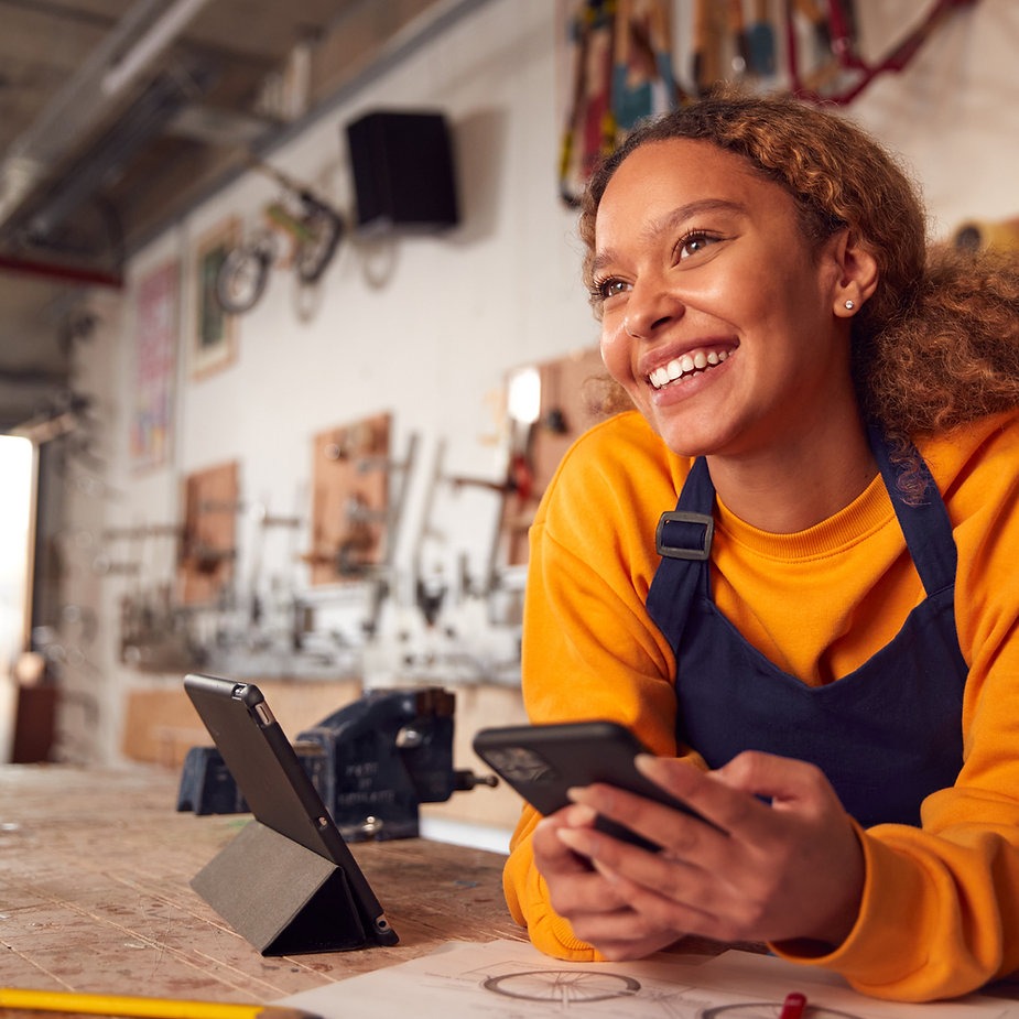 Smiling woman in a workshop with phone, showcasing Emernplus services.